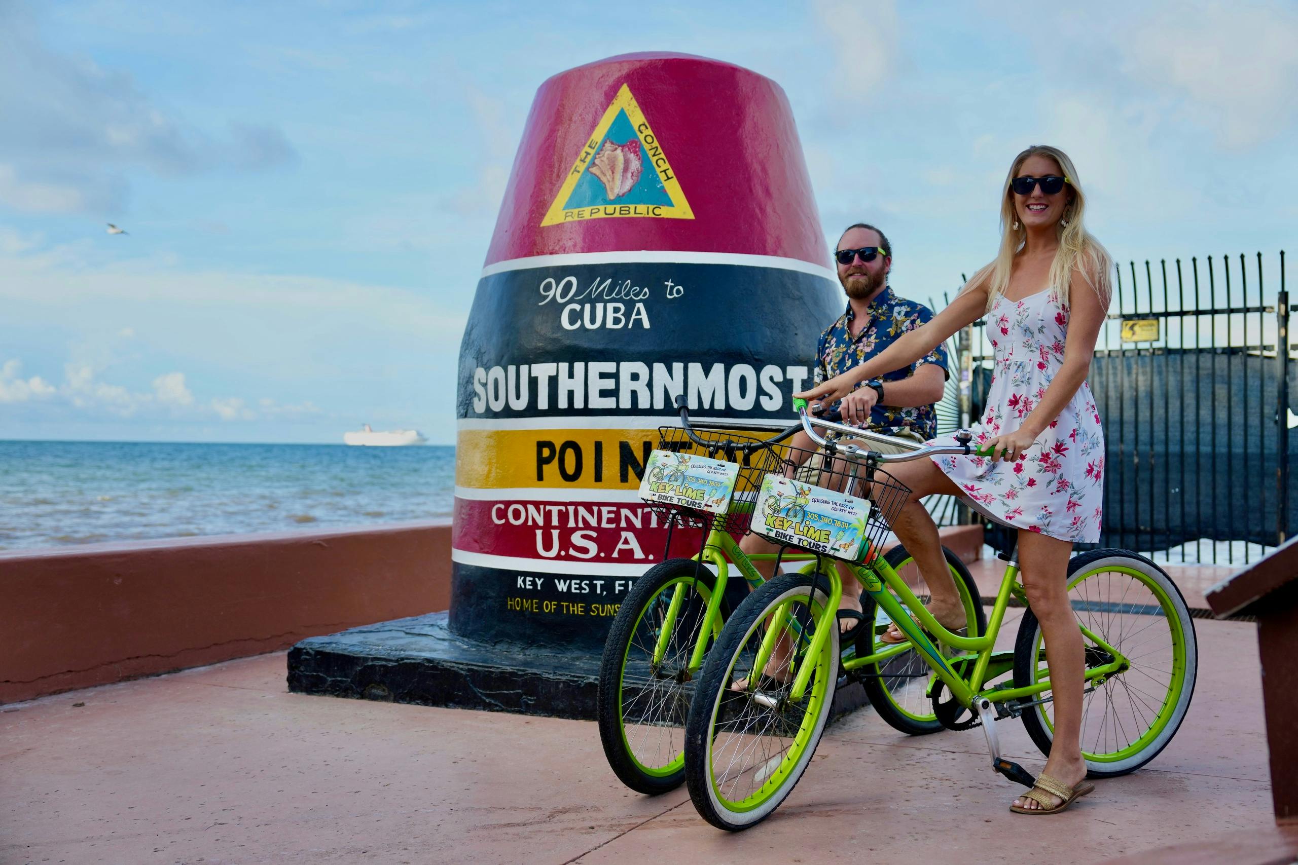 Un homme et une femme à vélo posant près de la bouée de Southernmost Point à Key West, en Floride.