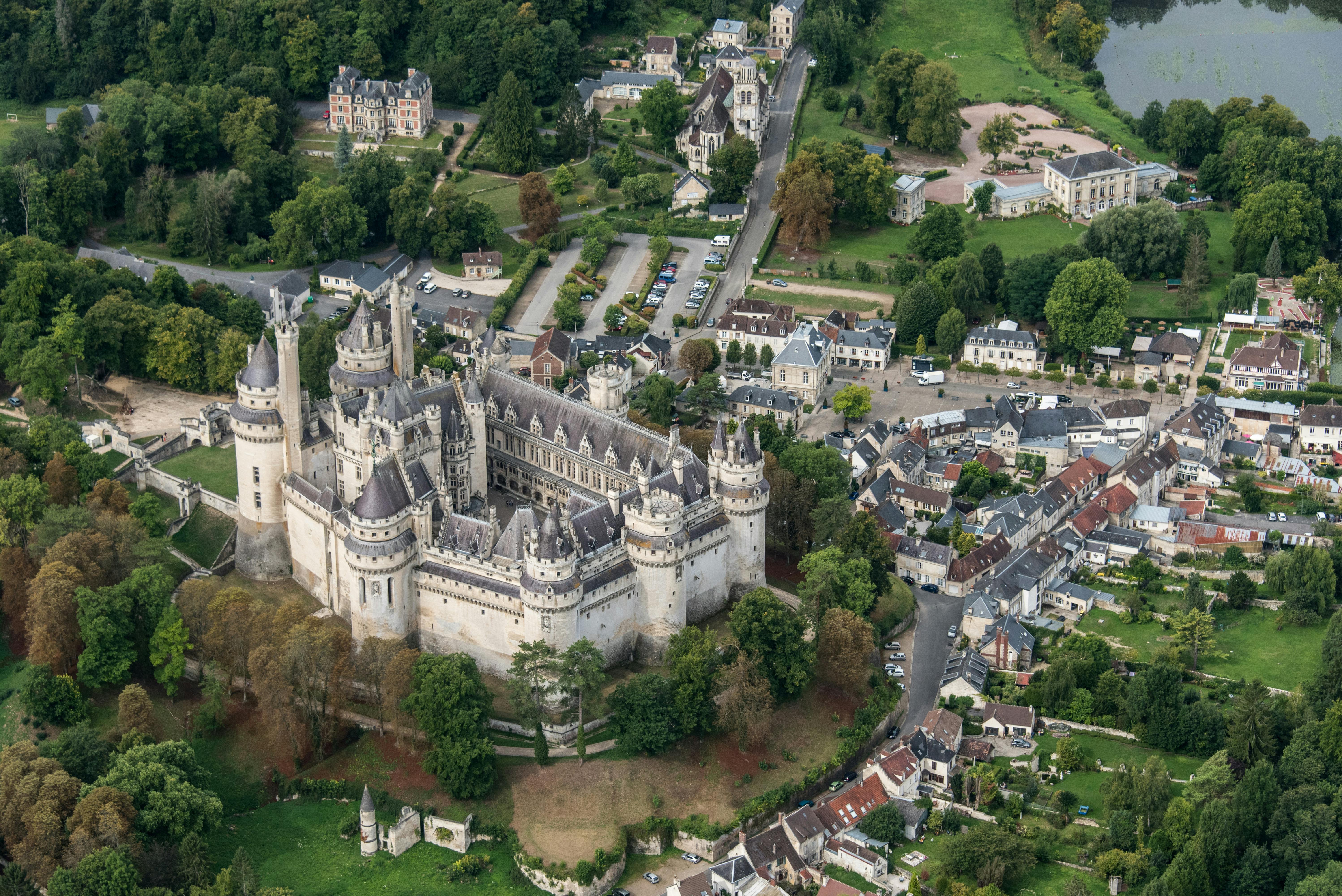 一座中世纪风格的大型城堡，四周环绕着树木、小建筑和道路，坐落在古朴的村庄环境中。