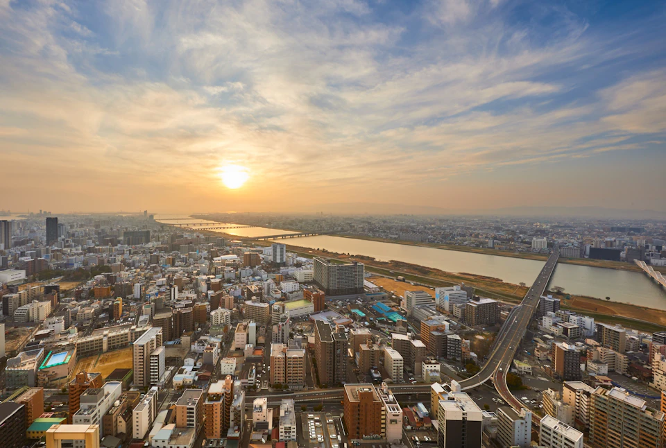 Aerial view of a cityscape at sunset with a river running through it, surrounded by buildings and roads.