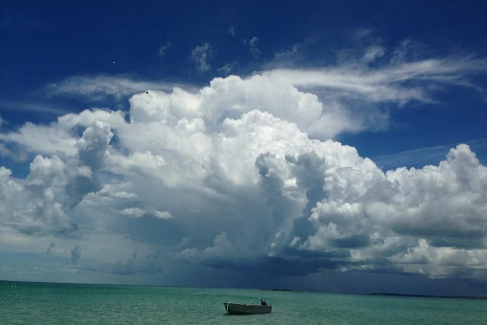 A small boat floating on calm turquoise water under a dramatic sky with large, billowing clouds.