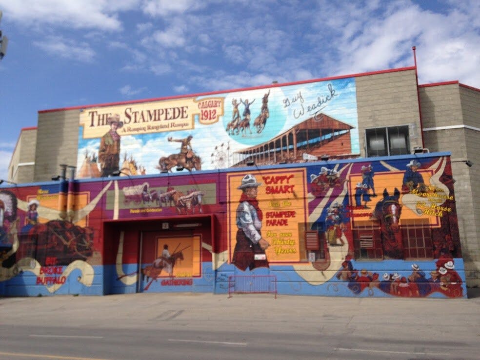 Facciata dell&#39;edificio con murales colorati di cowboy, cavalli e scene di rodeo che promuovono il Calgary Stampede con il testo &#34;Stampede&#34;.