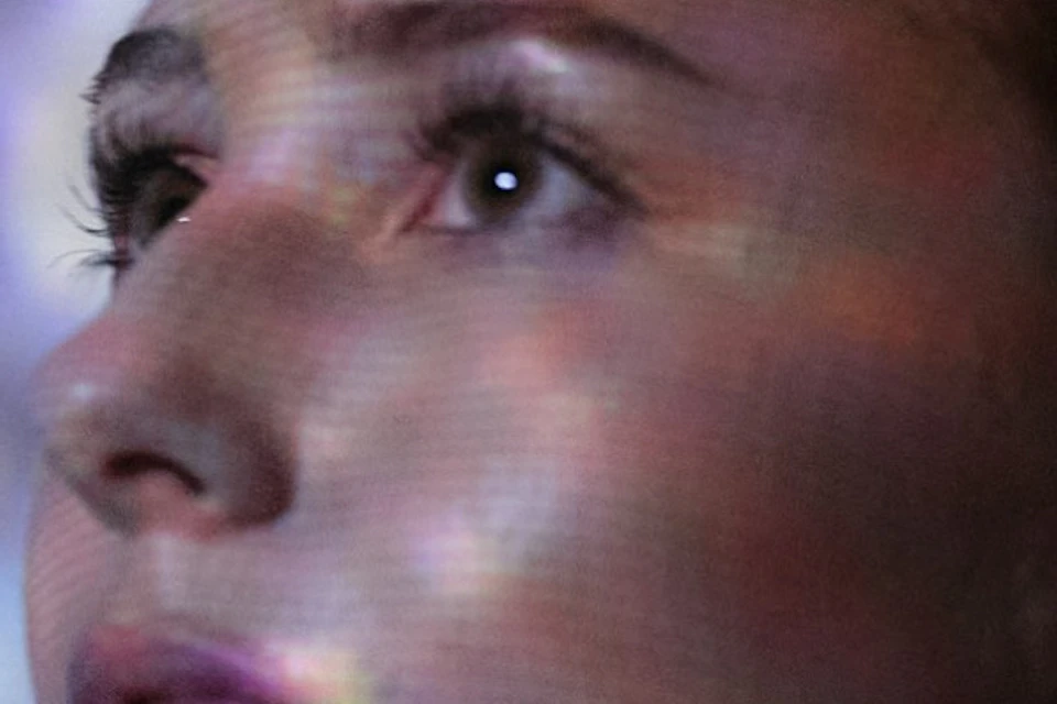 A woman with light brown hair looks upward, a starry projection casts patterns on her face and the background.