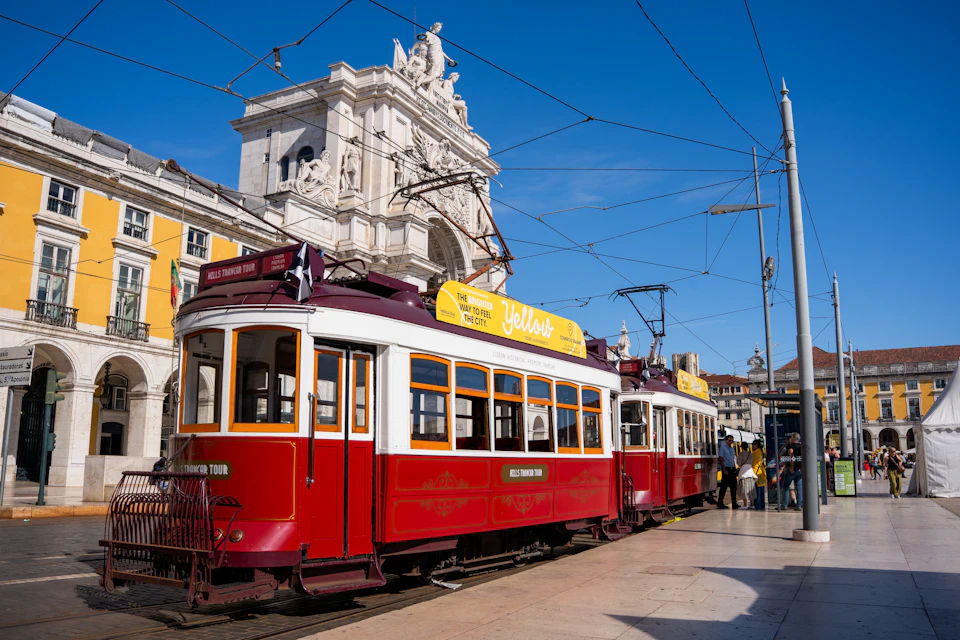 A red and white tram with a yellow advertisement stopped in front of a historic building under a clear blue sky.