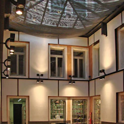 En modern innergård med ett geometriskt glastak, flera fönster, spotlights, en central brunn och skyltfönster i glas.