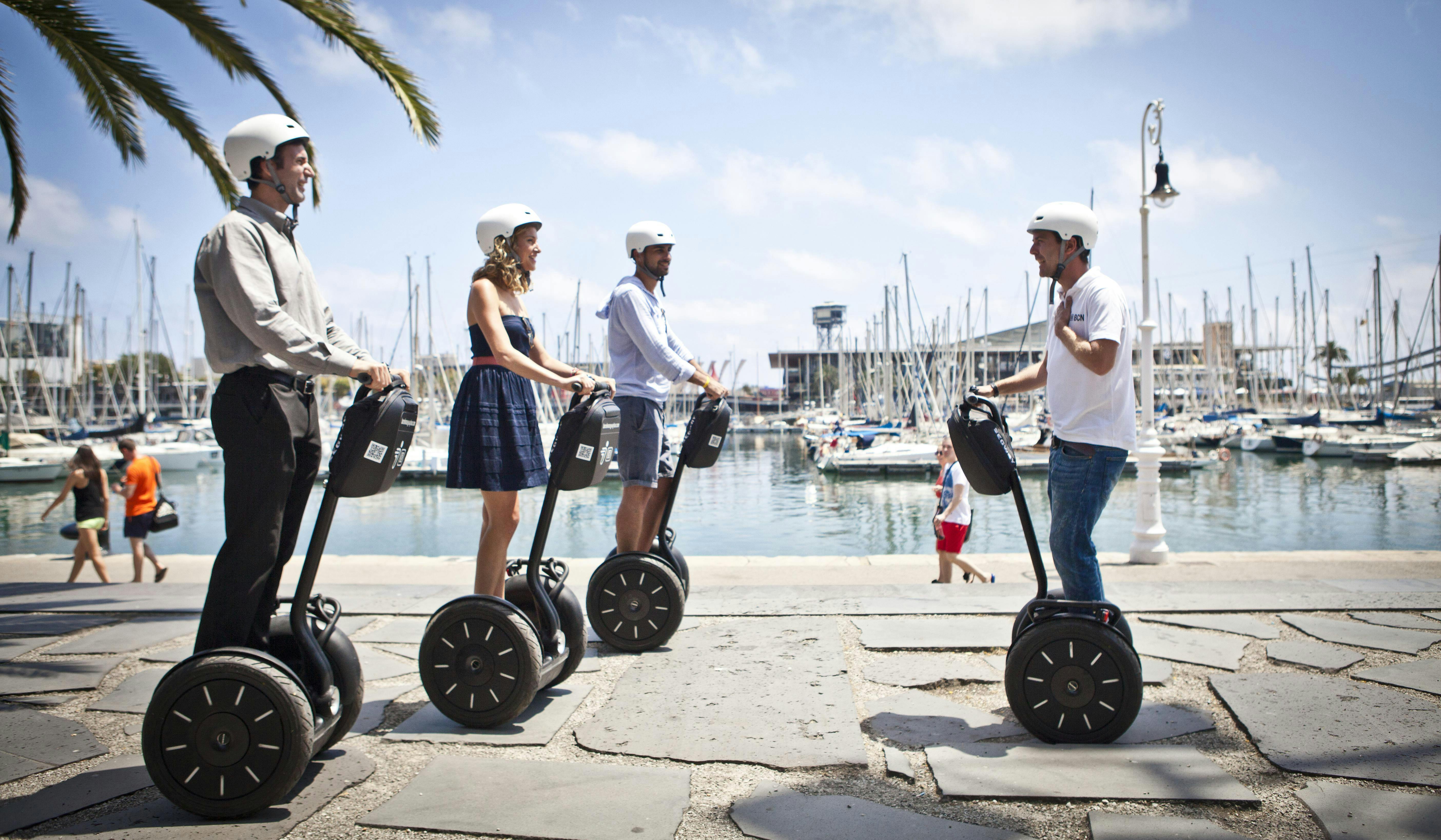 Trois personnes portant des casques conduisent des Segway le long d'un front de mer bordé de bateaux et de palmiers, sous un ciel dégagé.