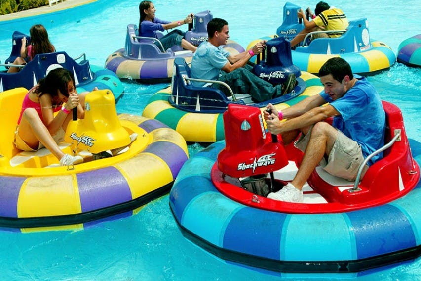 Des personnes dans des bateaux tamponneurs colorés naviguant sur un manège aquatique, souriant et profitant de l'activité.