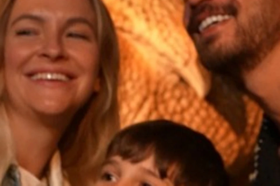 Three people pose for a photo in front of a dinosaur model in a dimly lit setting.