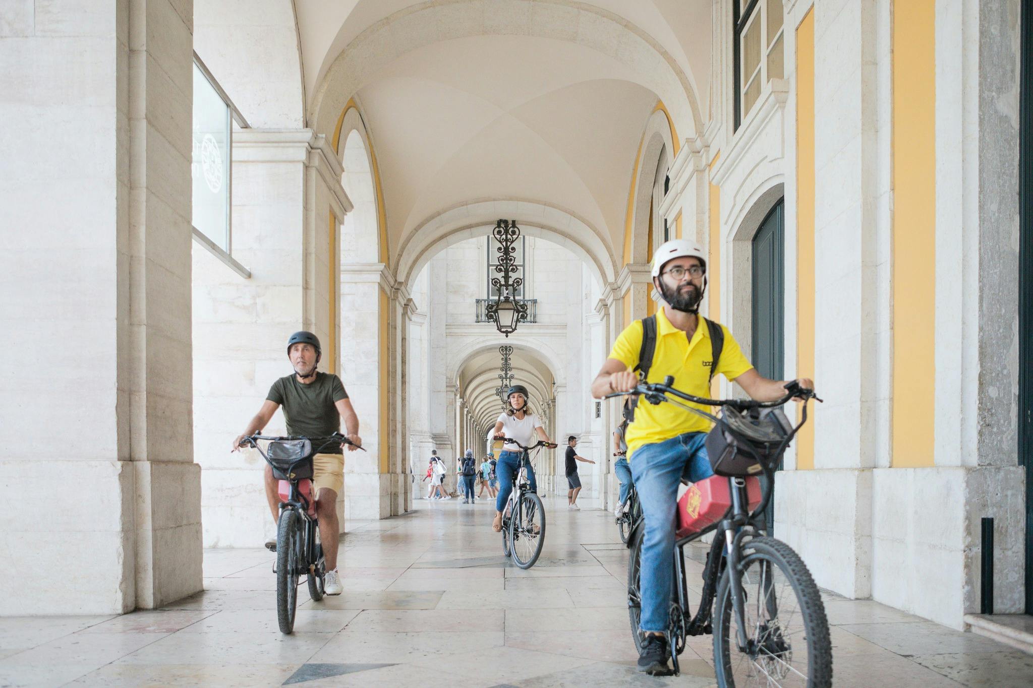 Touristes profitant d'une visite en E-Bike à Lisbonne, avec un arrêt à la place du Commerce.