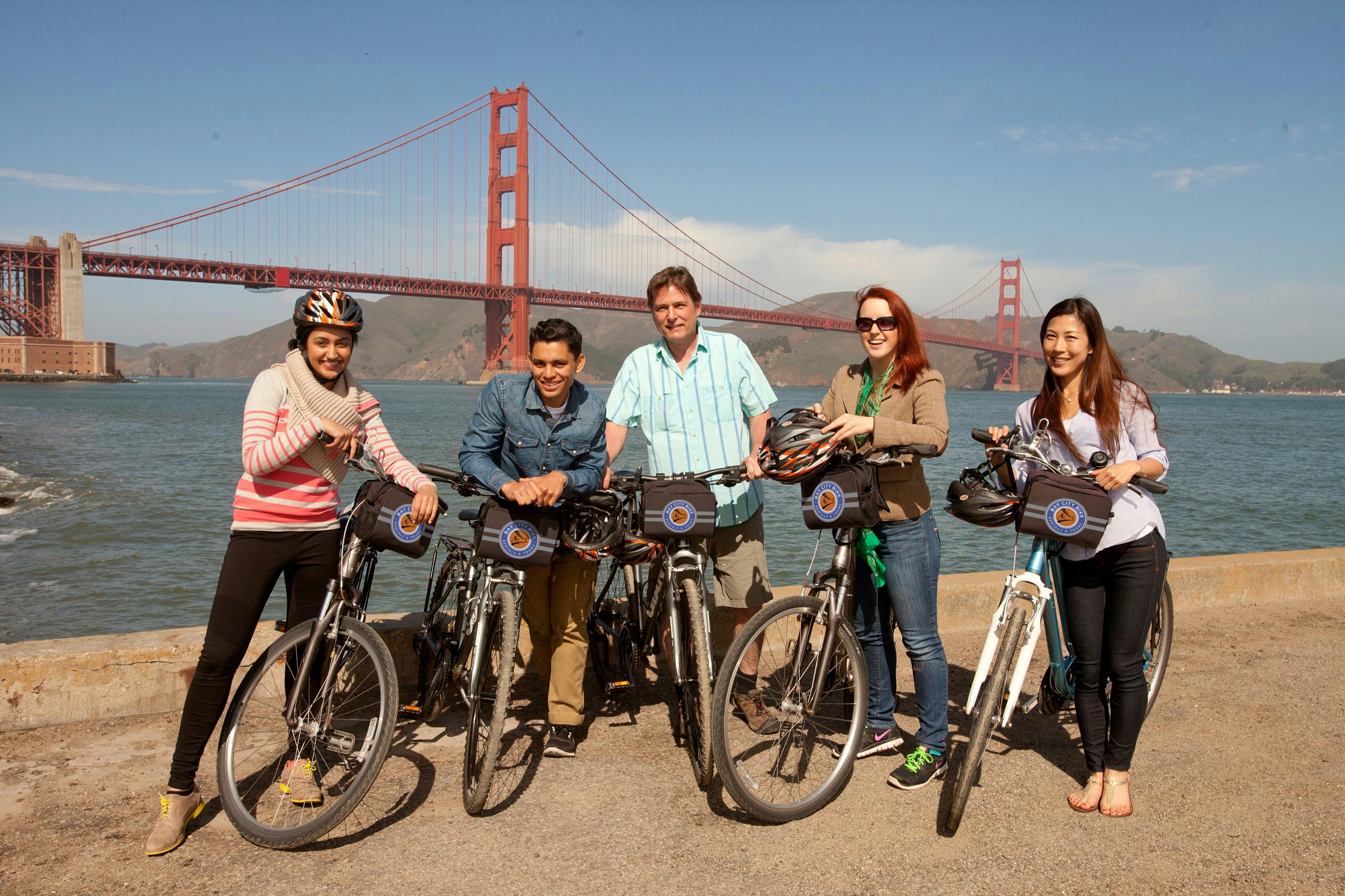 Four people standing with bicycles in front of the Golden Gate Bridge under a clear sky.