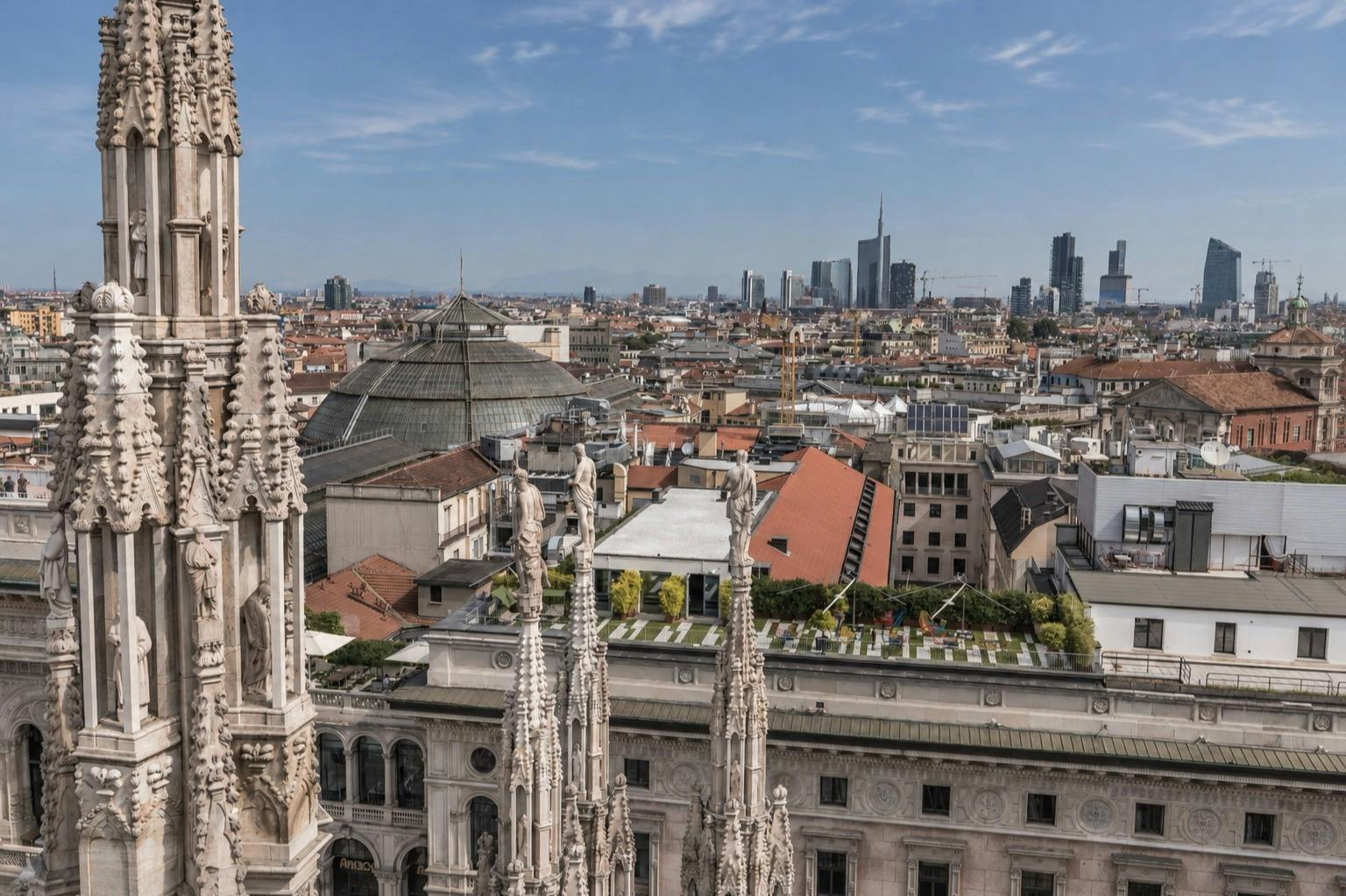 View of a cityscape from a cathedral rooftop, with decorative spires in the foreground and modern buildings in the distance.