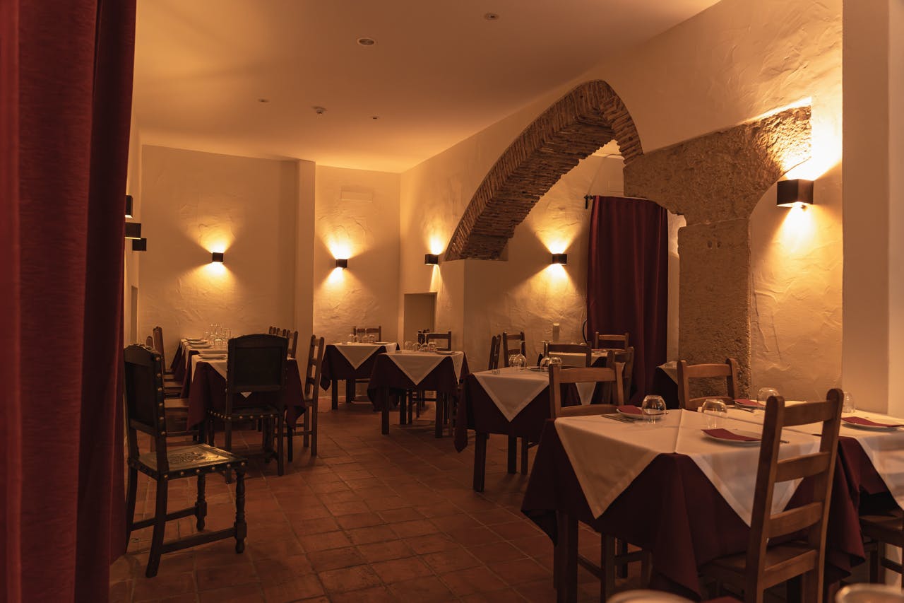 栗色のカバーに白いテーブルクロスを掛けた薄暗いレストラン、木製の椅子、壁の壁掛けで照らされたアーチ型の玄関口。