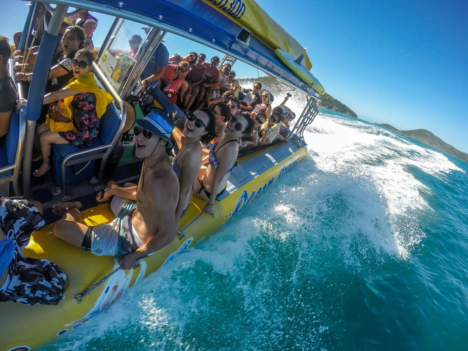 A group of people riding a yellow boat on the water, enjoying a sunny day with waves splashing nearby.