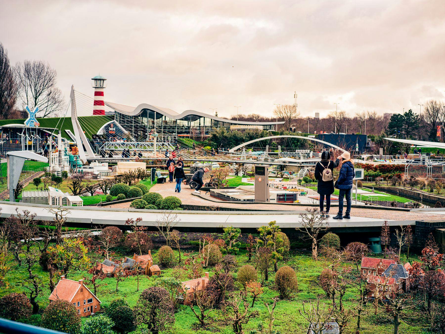 緑豊かな緑、ミニチュアビル、灯台がある公園のようなエリアに住む人々。 歩行者のいる通路が見える。