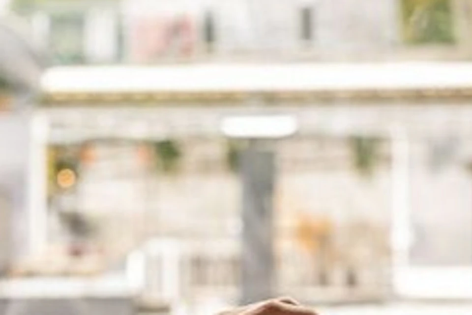 A man in a white shirt pours champagne at a table adorned with rose petals, glasses, and a menu, with an outdoor cityscape in the background.