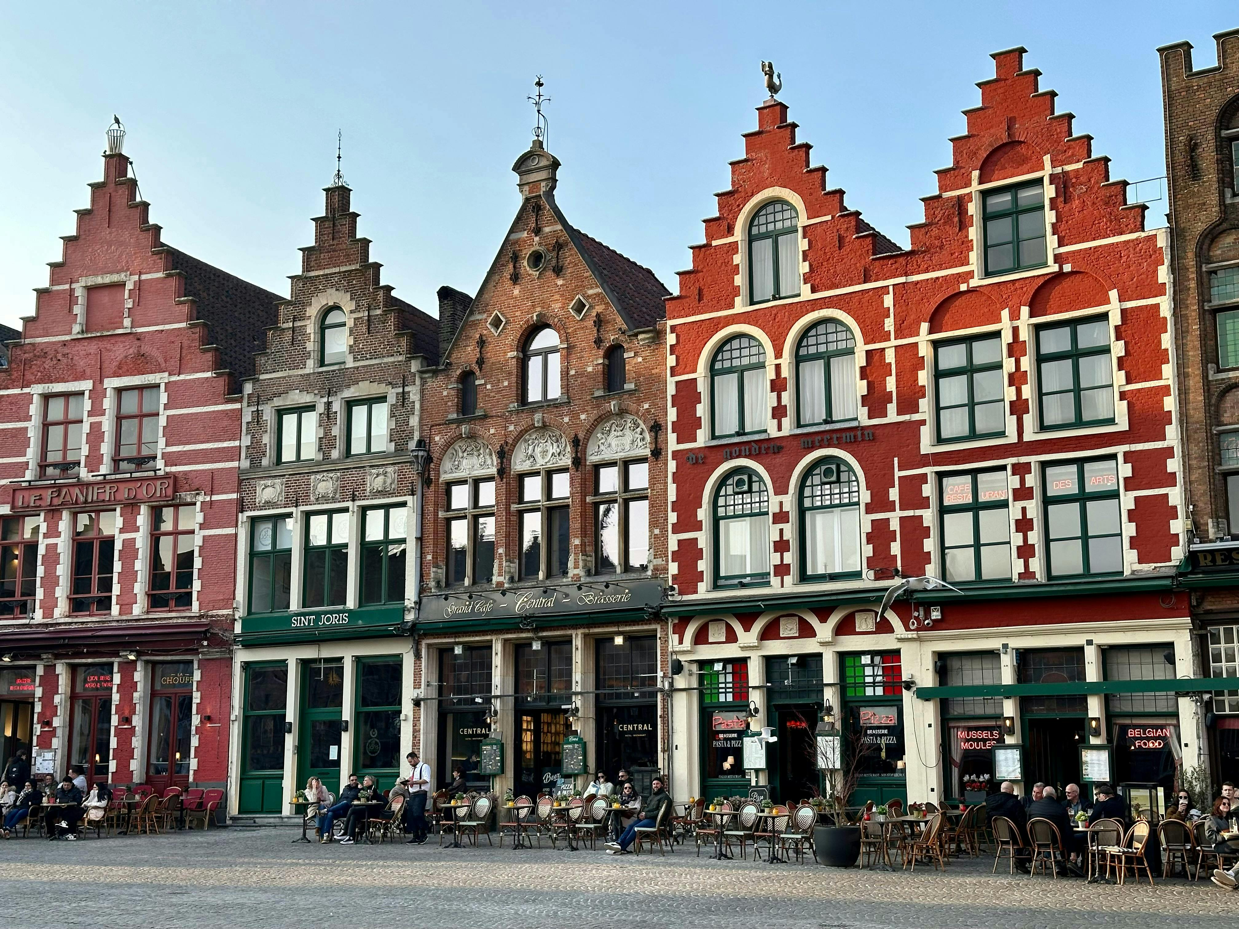 A street scene featuring colorful historic buildings with stepped gables, outdoor seating, and cobblestone pavement.