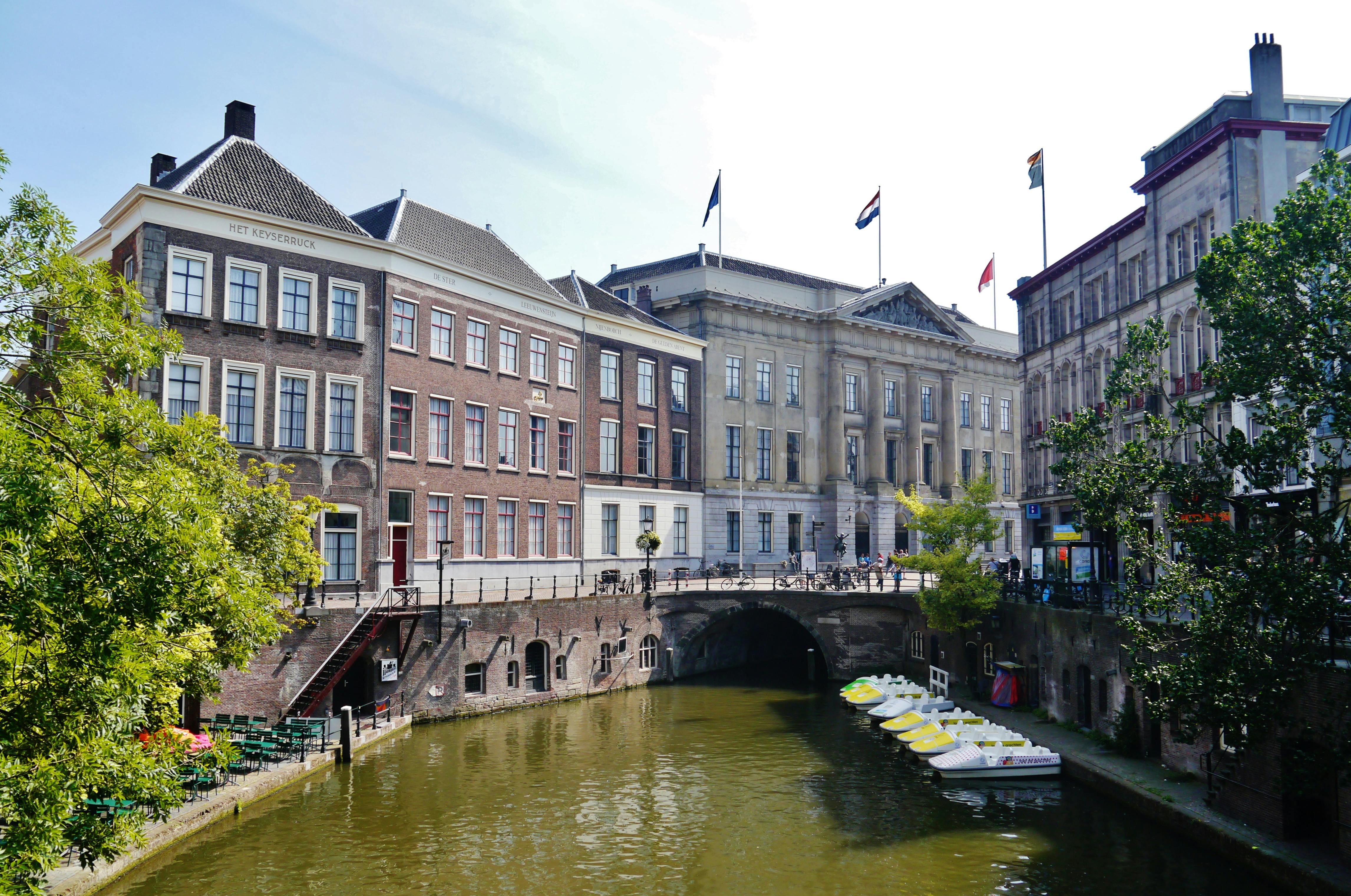 運河沿いに駐車された自転車は、歴史的建造物とアーチ型の橋が背景に並んでおり、水上にパドルボートが停められています。