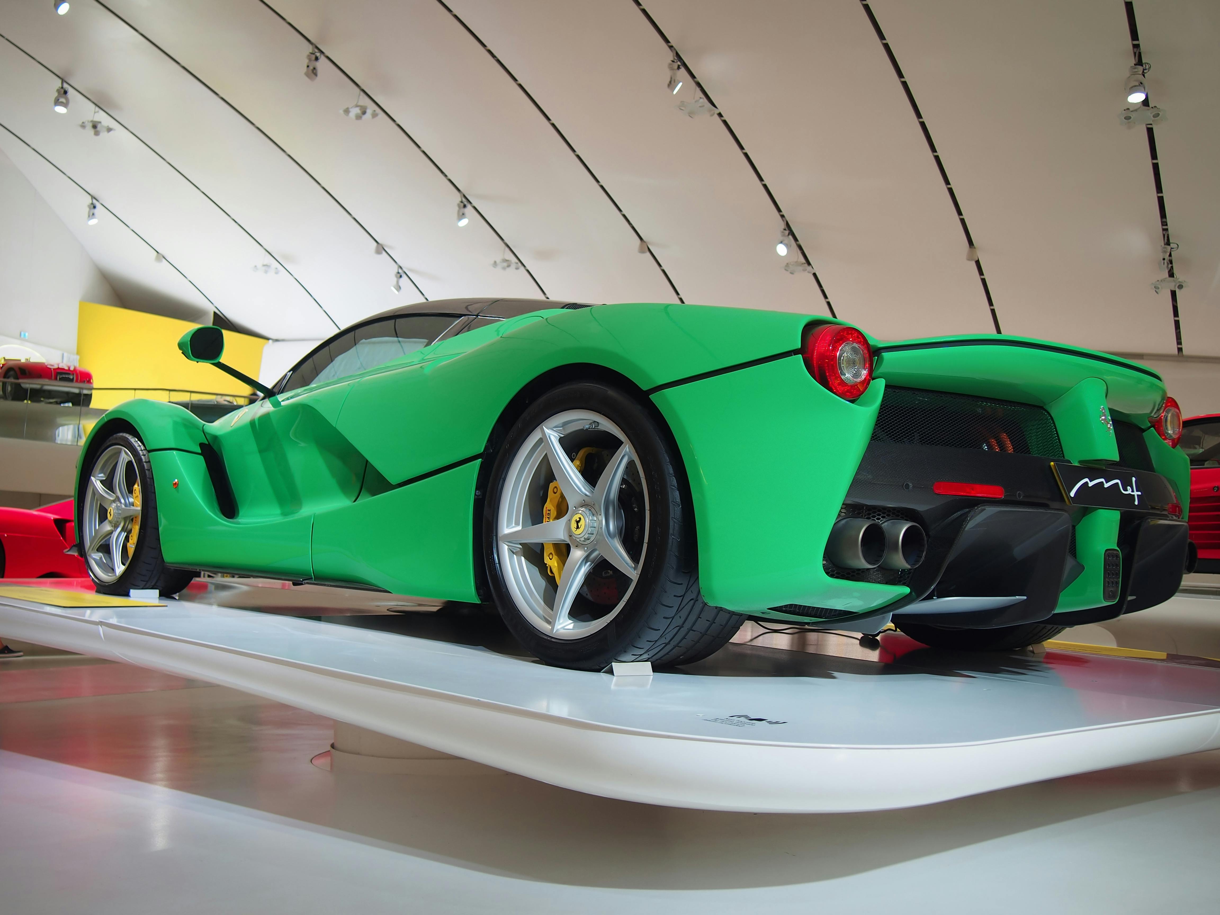 Ένα πράσινο σπορ αυτοκίνητο με ασημί τροχούς εμφανίζεται σε εσωτερικούς χώρους κάτω από μια καμπύλη, μοντέρνα οροφή με φώτα.