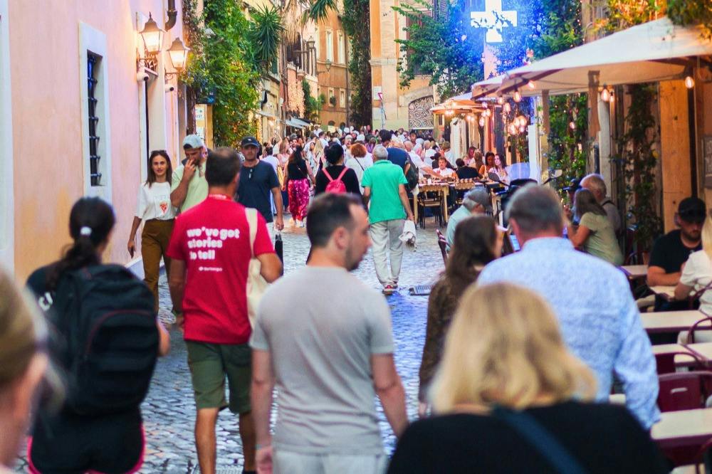 A lively pedestrian street with people walking and dining, lined with buildings, trees, and outdoor seating.