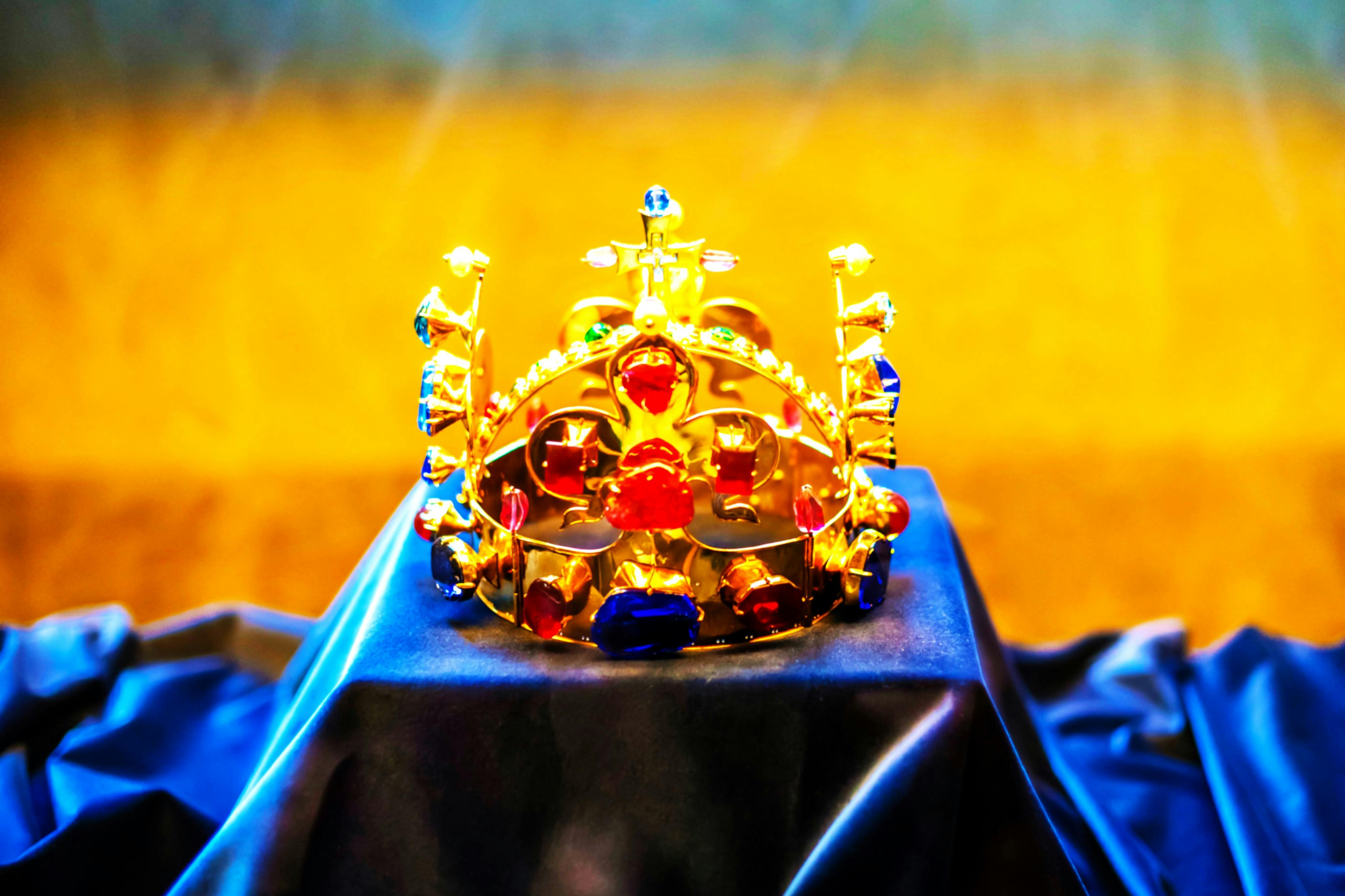 A golden crown adorned with colorful jewels displayed on a dark cloth.