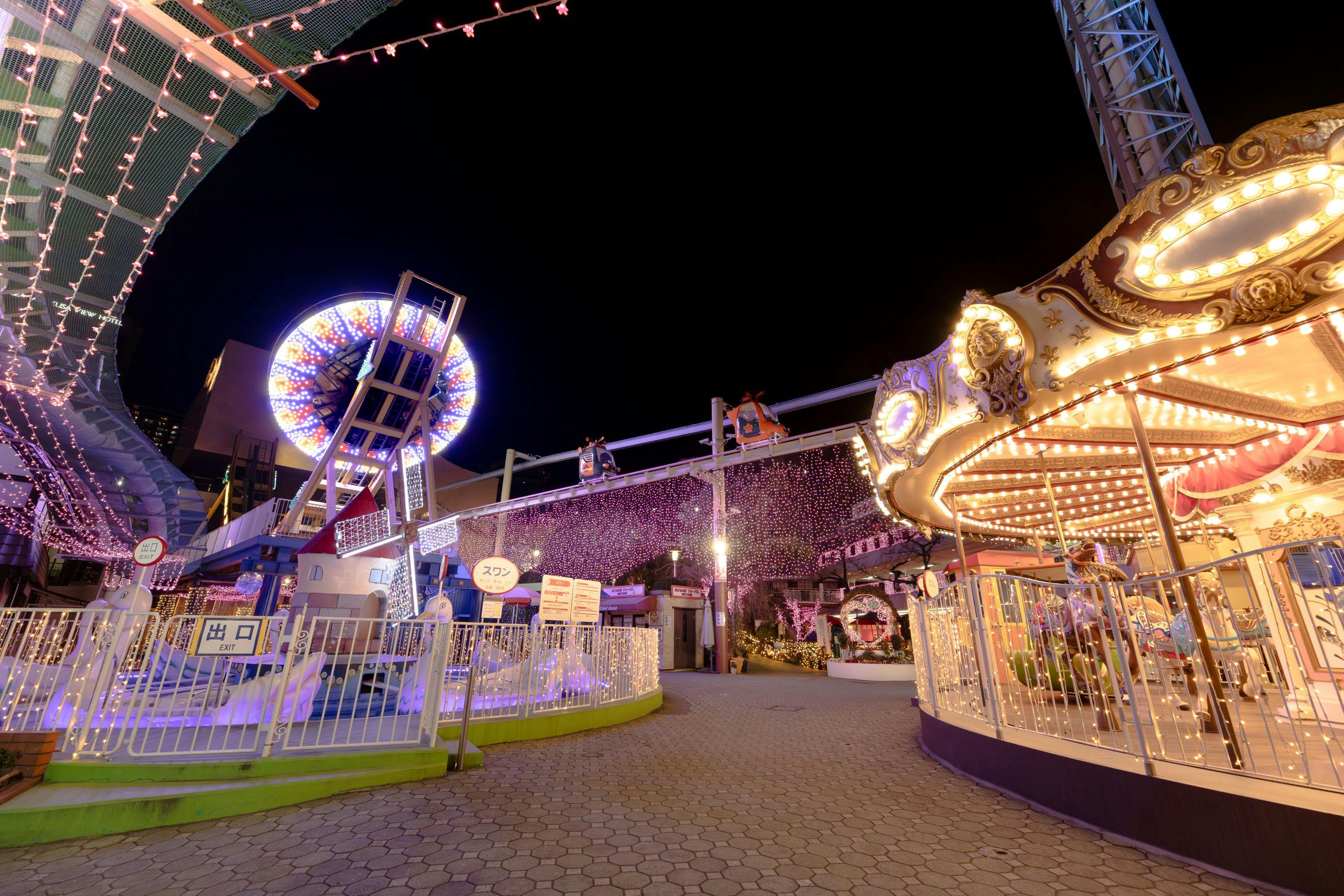 An amusement park at night, featuring a carousel, a Ferris wheel, and decorative lights creating a festive atmosphere.