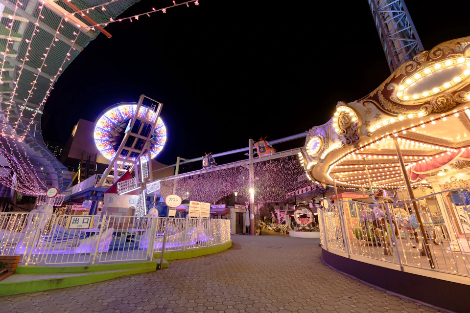 An amusement park at night, featuring a carousel, a Ferris wheel, and decorative lights creating a festive atmosphere.