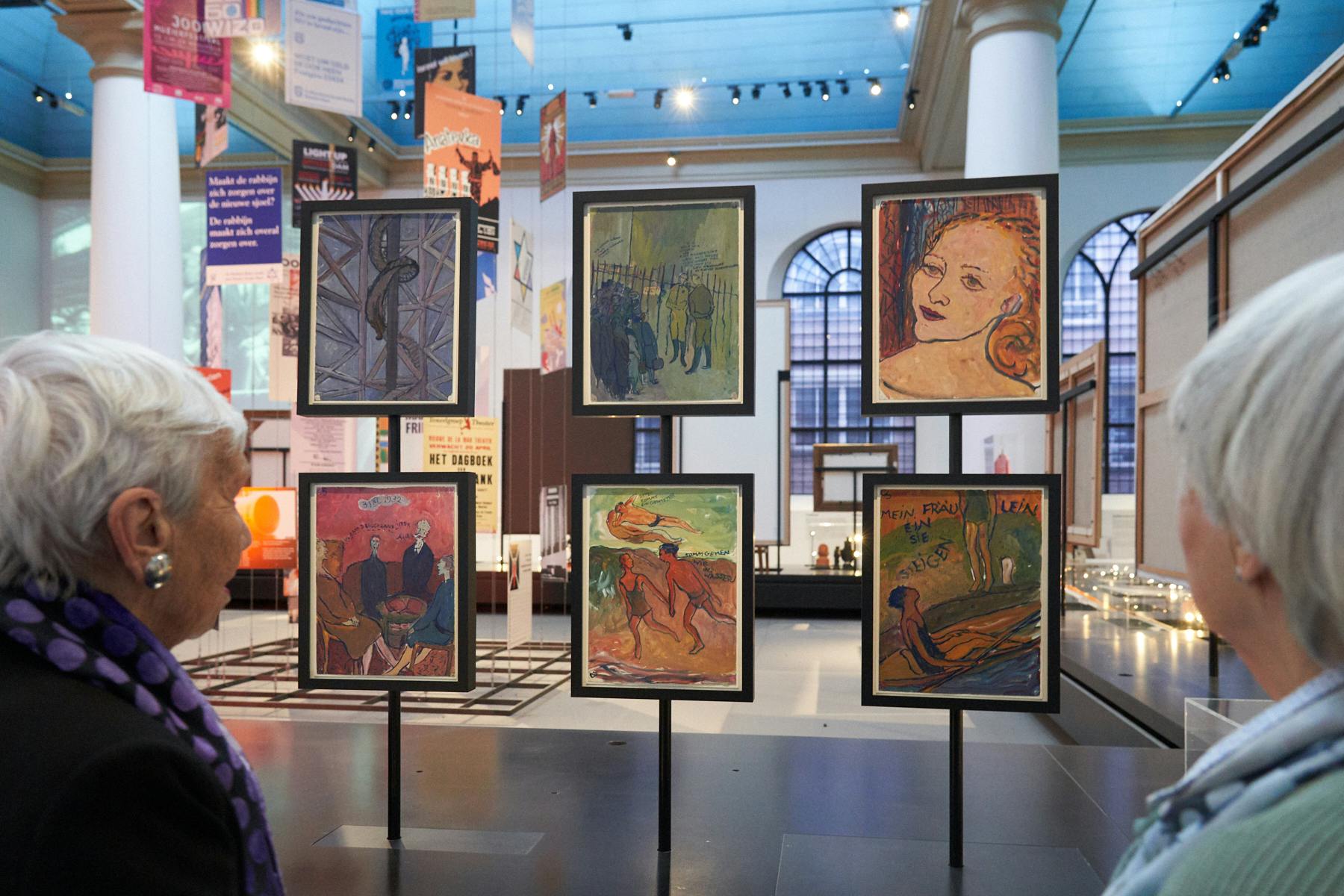 Personne regardant une œuvre d'art encadrée dans un musée, présentant quatre peintures colorées sur un support, sur fond de hautes fenêtres et de colonnes.