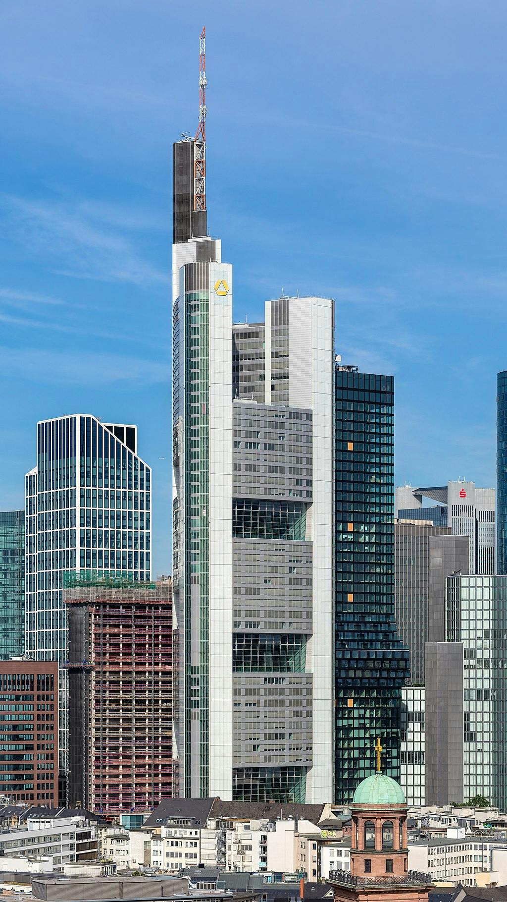Skyscrapers in downtown area with one prominent white and grey high-rise building featuring an antenna on top against a blue sky.