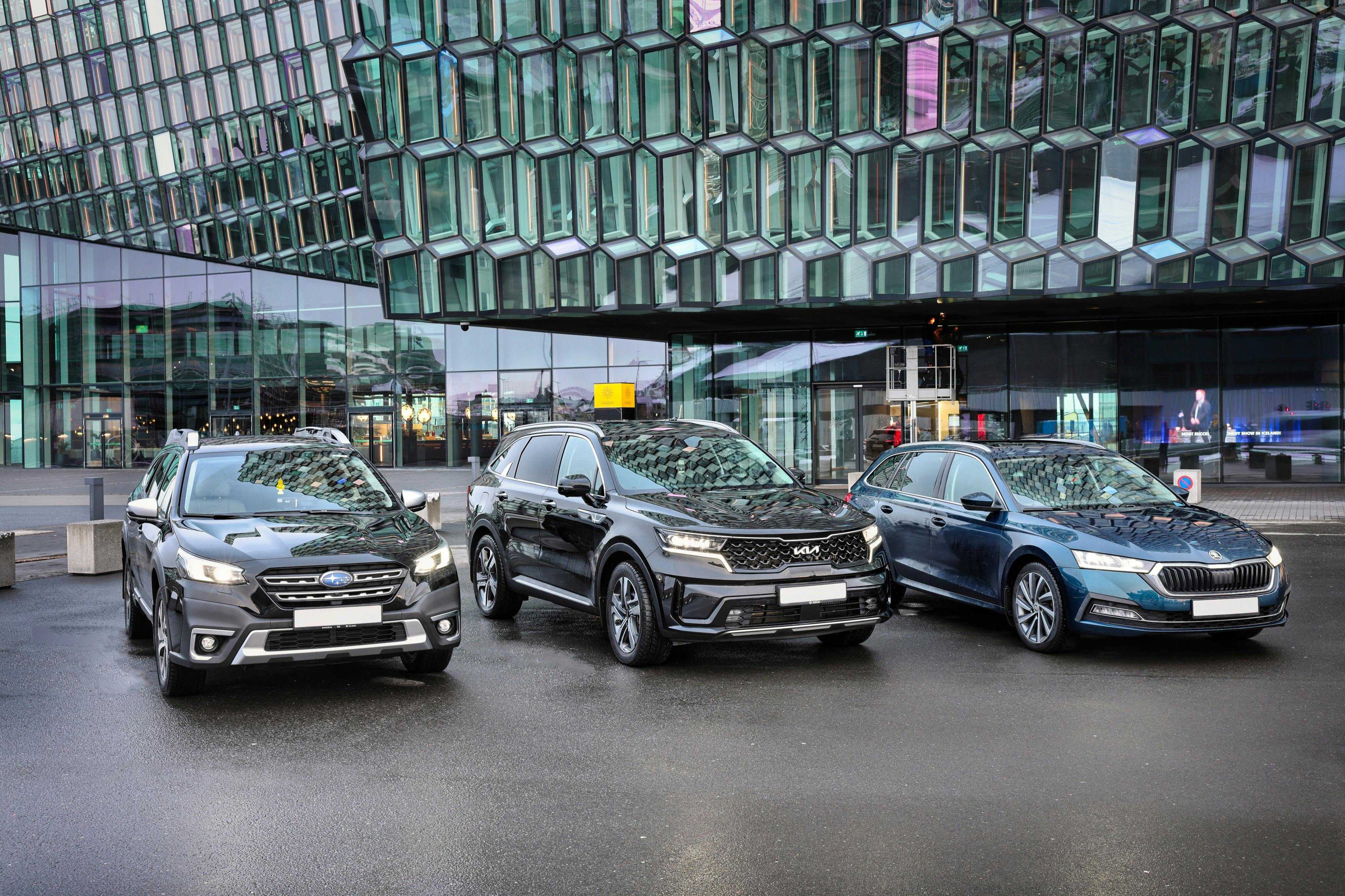 Three cars are parked in front of a modern glass building with a unique geometric facade.