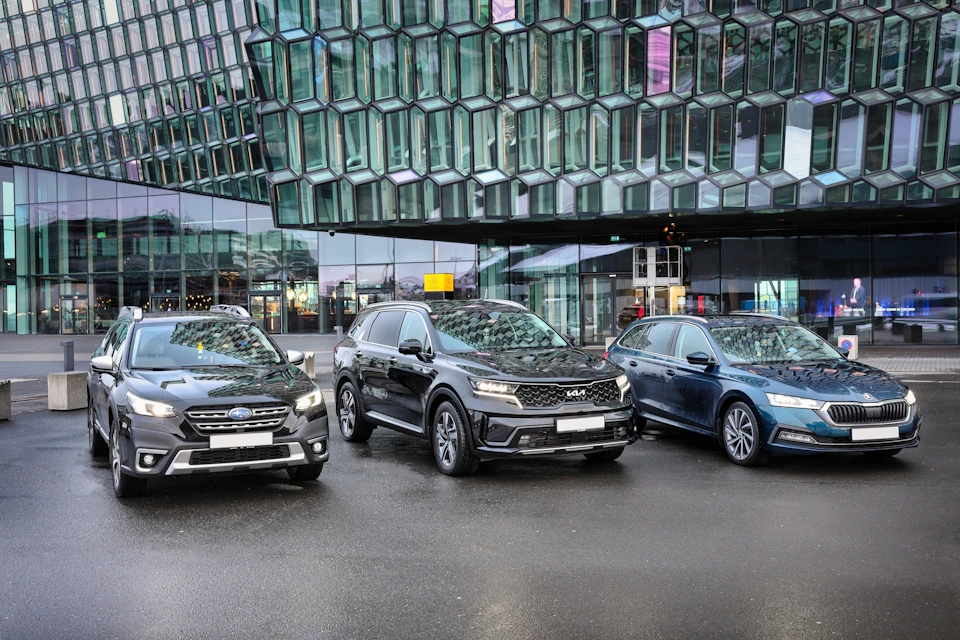 Three cars are parked in front of a modern glass building with a unique geometric facade.
