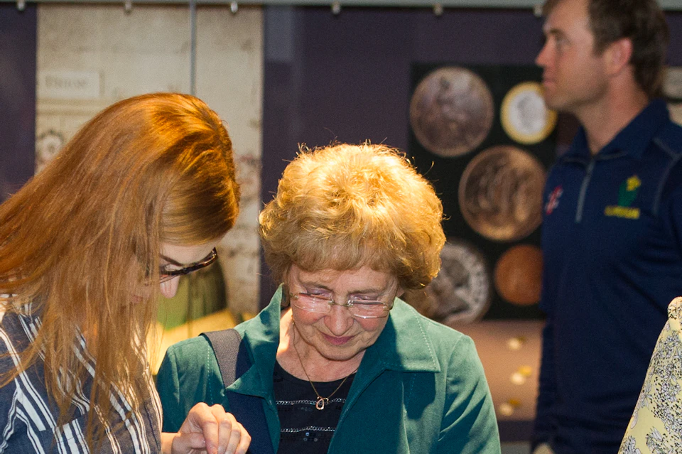 People interacting with a touch screen exhibit in a museum. Various displays and informational panels are visible in the background.