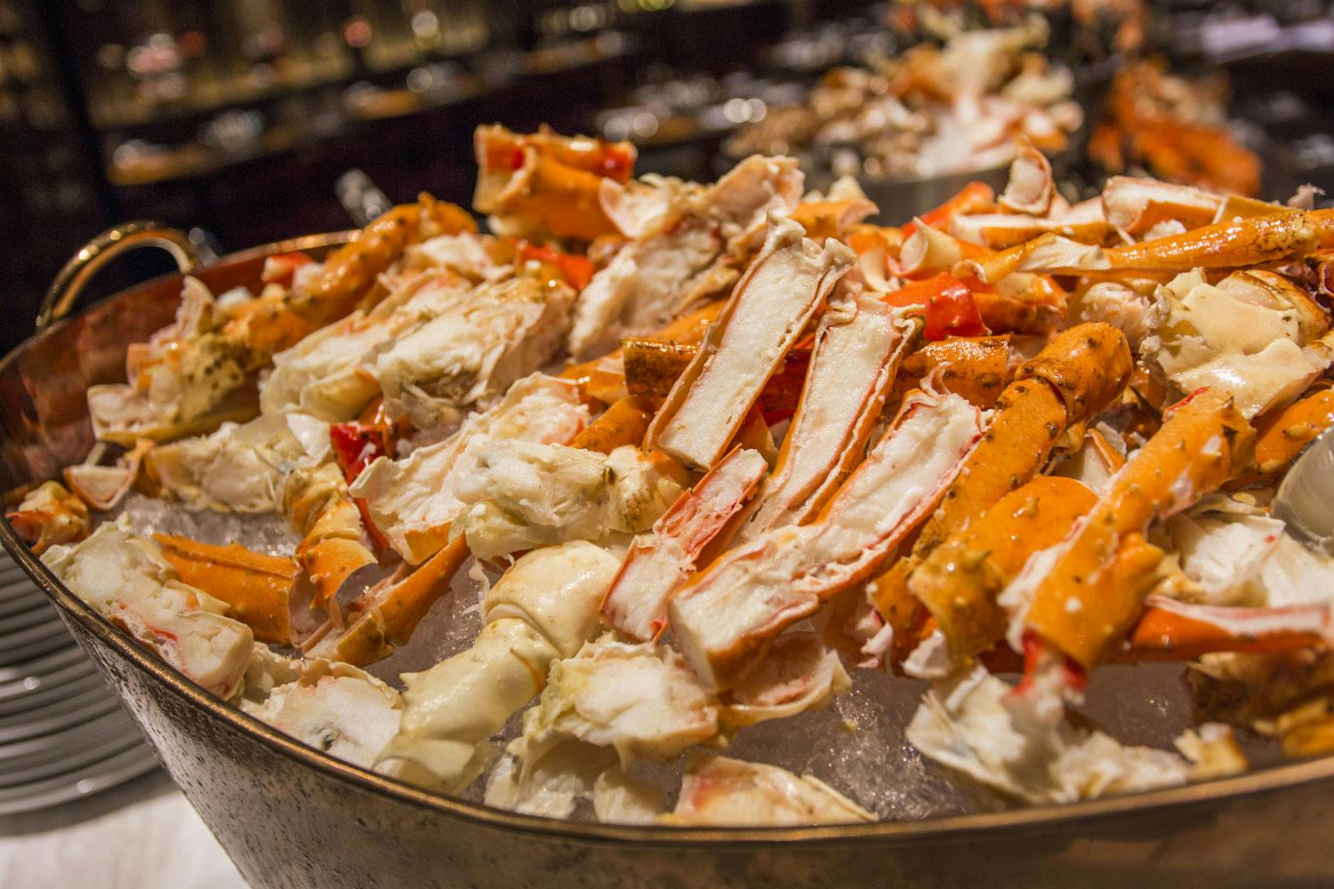 A heap of cooked crab legs and shells served on a bed of ice, displayed on a buffet table.