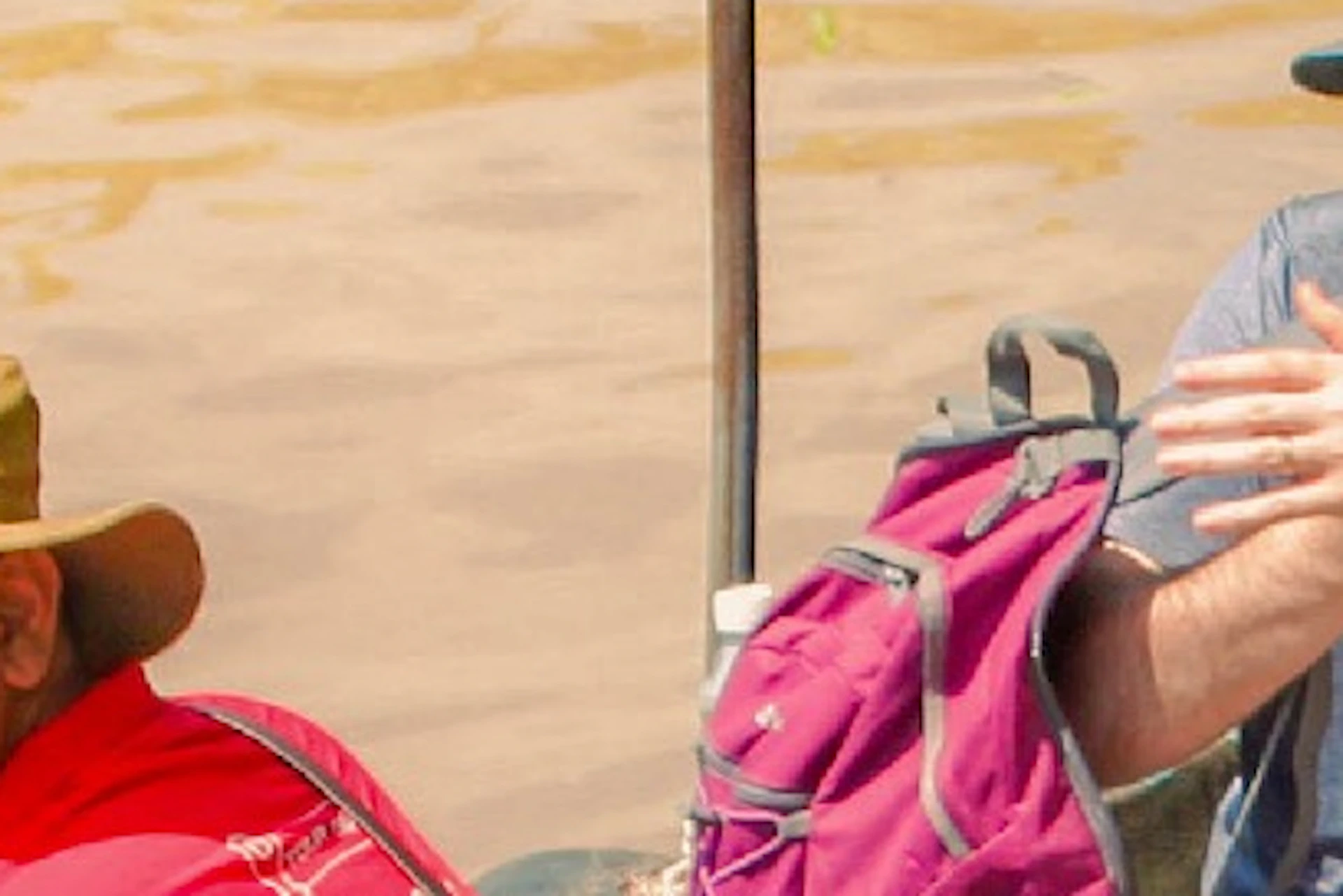 A boat with a guide and seated tourists navigating a muddy river near the bank.