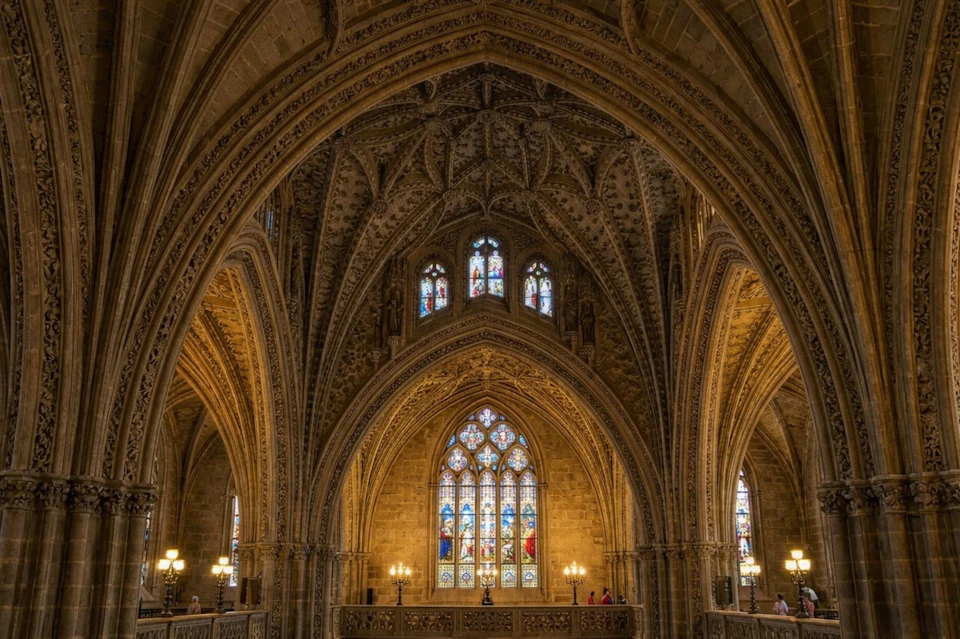 Intricate Gothic-style cathedral interior with arched ceilings and stained glass windows, lit by chandeliers and natural light.