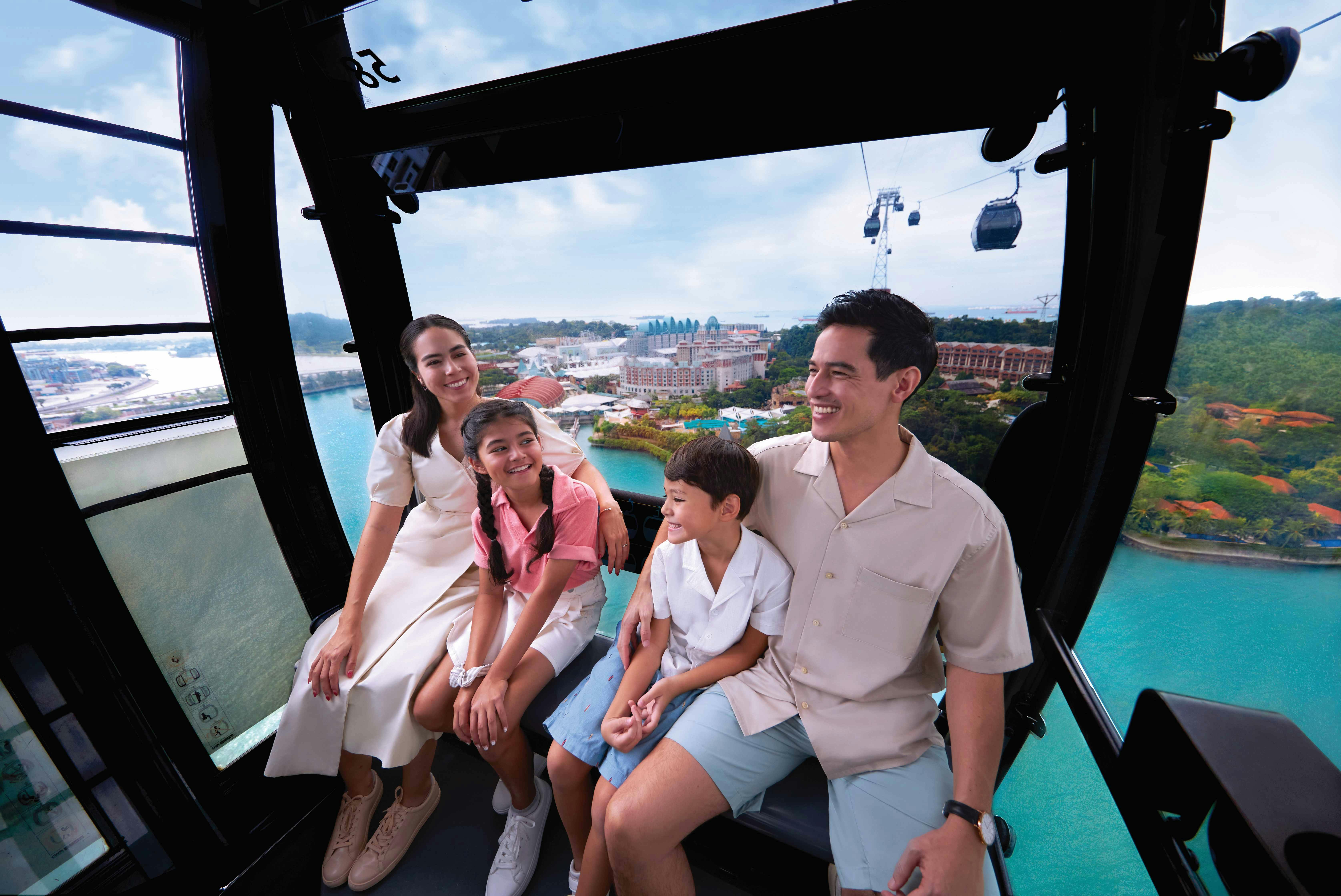 Μια τετραμελής οικογένεια χαμογελά μέσα σε ένα τελεφερίκ με μια γραφική παραθαλάσσια θέα στο παρασκήνιο.