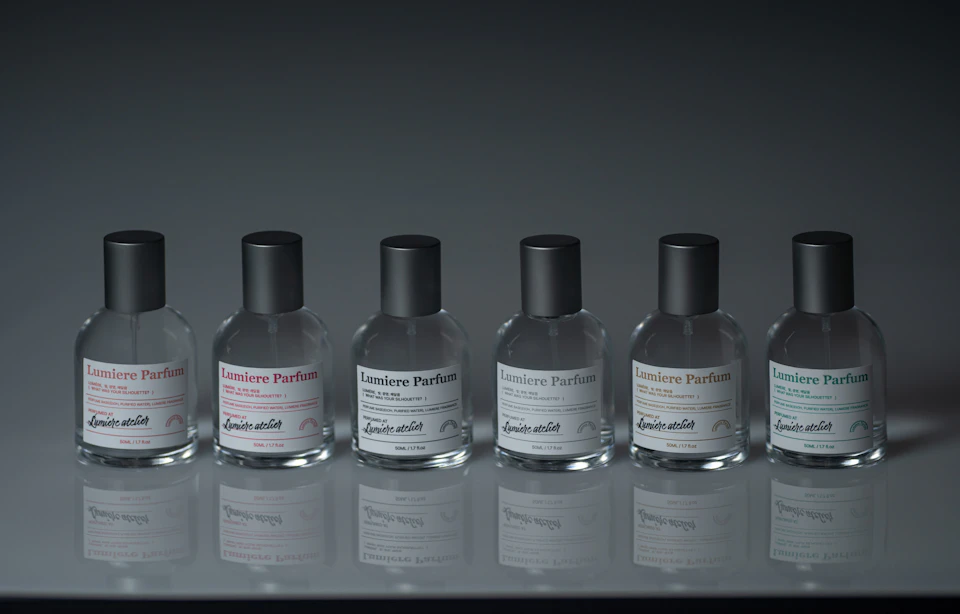 A row of six bottles of Lumiere Parfum with black caps and labels, placed on a reflective surface against a dark background.