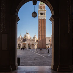 Visa igenom en valvgång på en torg med Basilica di San Marco och Campanile-tornet i Venedig, Italien. Folk går på torget.