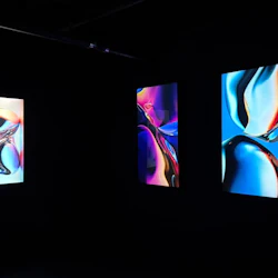 Tre vertikala abstrakta konstverk med levande färger som visas i ett mörkt rum.