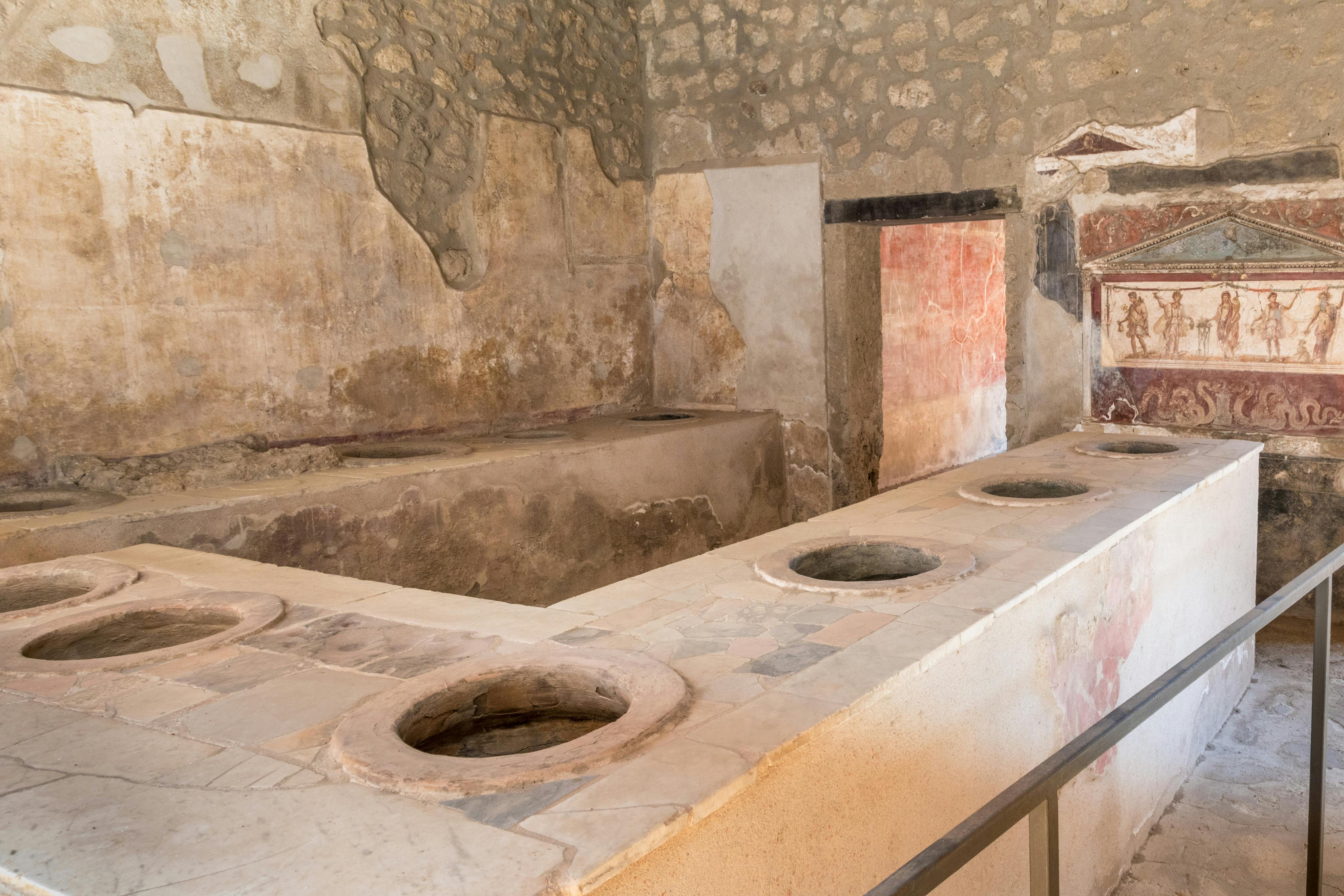 カウンタートップにいくつかの円形の穴、石の壁、フレスコ画や塗装された石膏の残骸がある古代の石造りのキッチン。