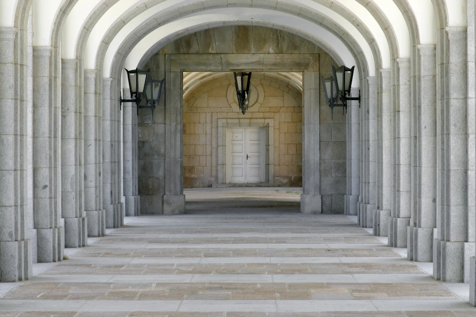 Stone archway with lanterns leads to a white double door framed by another arch inside a building.