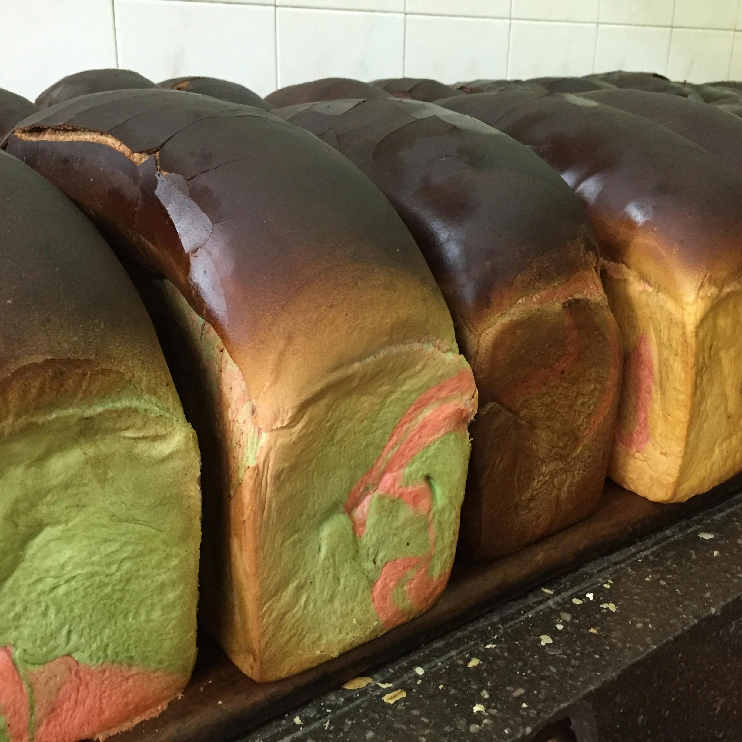 베이킹 트레이 위에 갈색 상판과 초록색과 분홍색 소용돌이가 늘어서 있는 빵 덩어리.