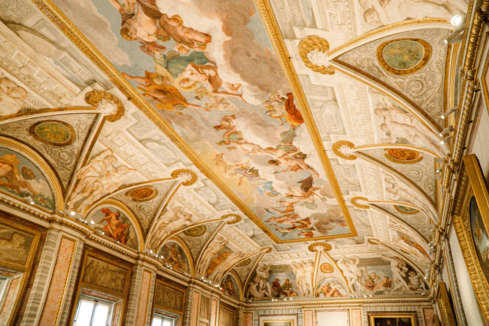 Ornate ceiling with detailed frescoes of mythological figures, surrounded by rich architectural details and golden accents.