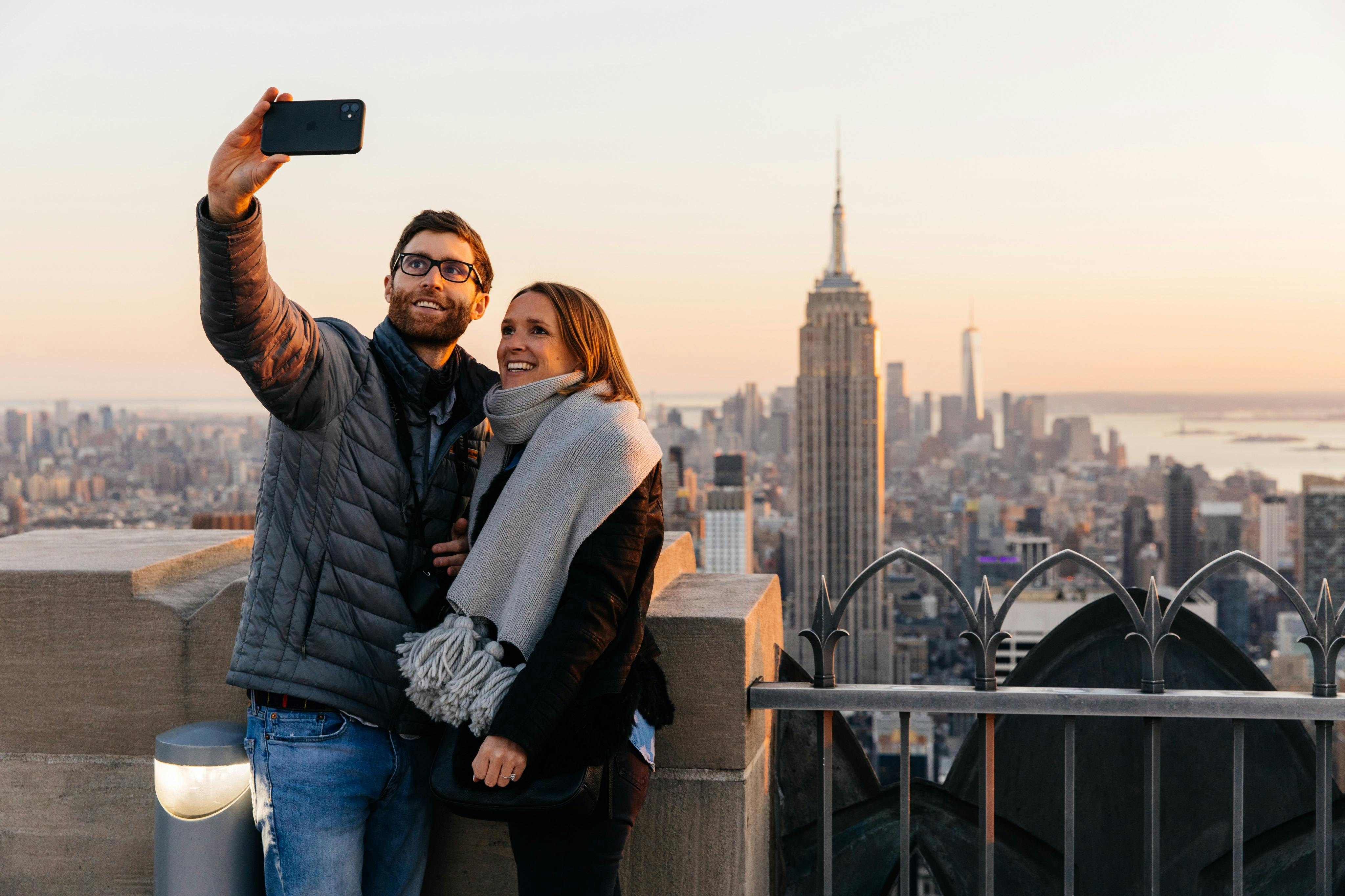 Um casal a tirar uma selfie num miradouro da cidade, com o Empire State Building visível ao fundo.