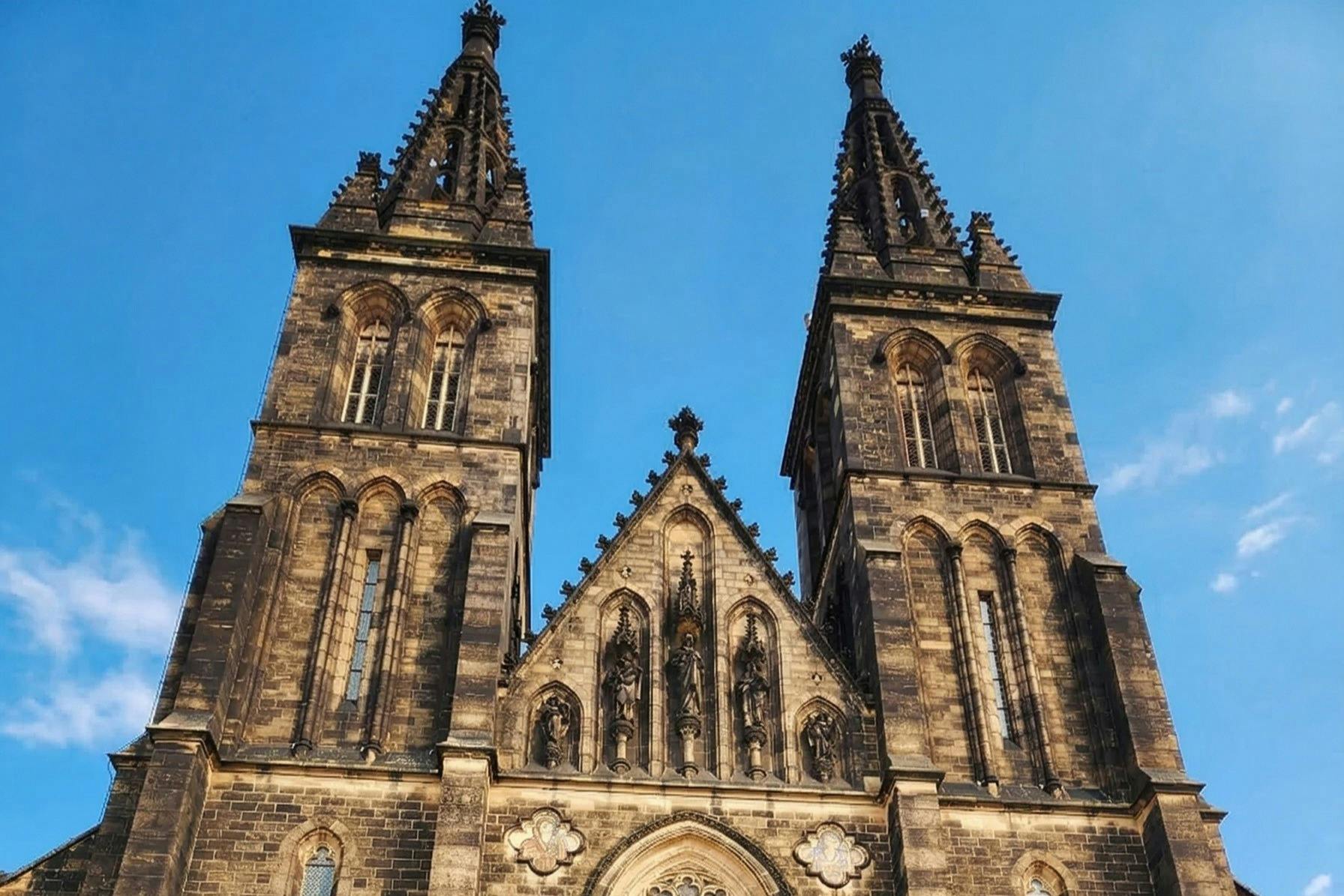 A Gothic-style church with two tall spires and intricate stone carvings, set against a clear blue sky.
