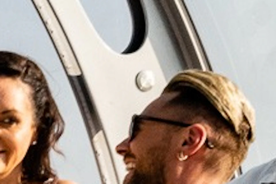 A group of people socializing in a glass-enclosed observation pod with a scenic view of the coastline and sky.