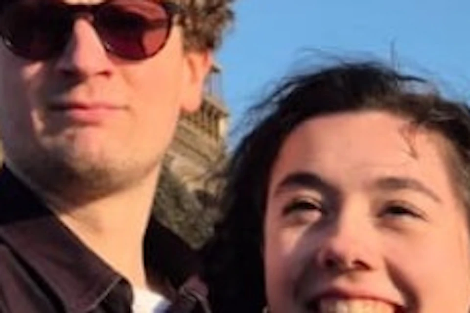 Two people taking a selfie in front of the Eiffel Tower on a clear day.