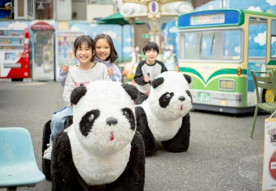 Children smiling while riding on large panda-shaped motorized toys in an amusement park setting.