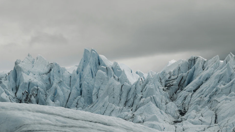 Jagged icy peaks of a glacier under a cloudy gray sky.