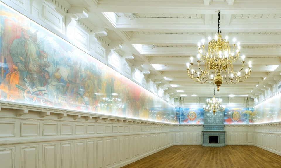 Elegant room with high ceilings, chandeliers, a long mural on the wall, white paneling, and wooden floors. No people present.