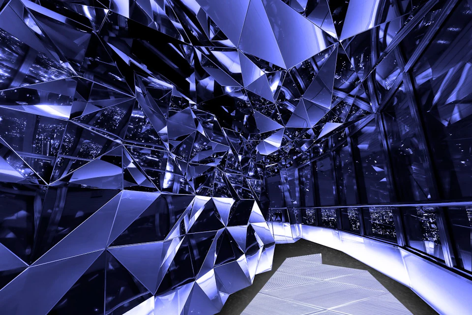 A room with reflective, angular mirrored surfaces creating a geometric and futuristic aesthetic, illuminated in blue light.