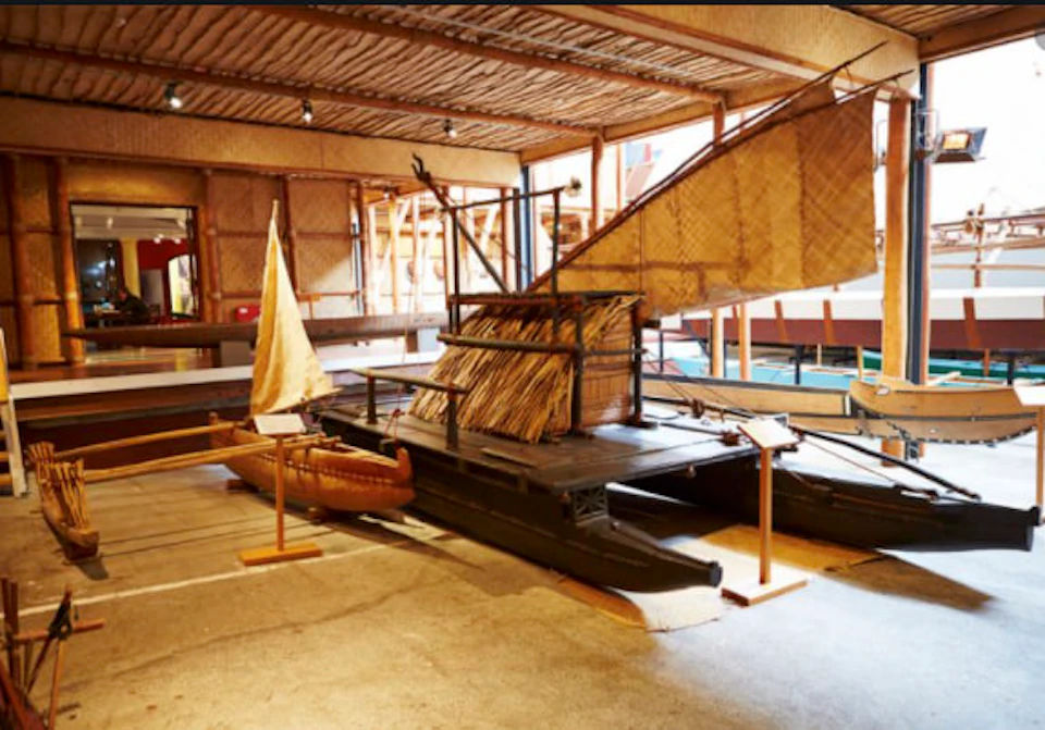 A traditional sailing canoe with woven sails and a thatched cabin displayed in a museum exhibit.